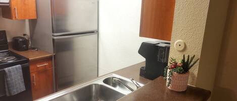A compact kitchen with stainless steel appliances, a sink, and a countertop with a potted plant.