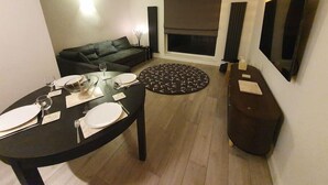 A modern living room with a dining table set for four, a sofa, a fireplace, and a large TV on the wall.