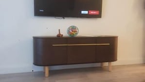 A modern living room with a flat-screen TV mounted on the wall displaying the Netflix logo, a wooden cabinet below, and a patterned rug on the floor.