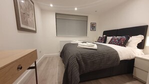 A modern bedroom with a bed, bedside tables, a desk, and a large window.
