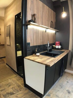 A modern kitchen with a wooden countertop, black cabinets, and a built-in sink. - Le TULUM, hyper center, place aux herbes (Mâcon)