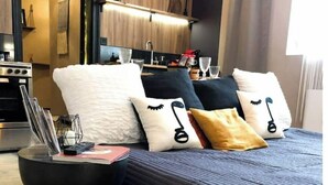Een moderne slaapkamer met een donkerblauwe sprei, meerdere kussens, een gebreide poef en een houten wand met een hanglamp.