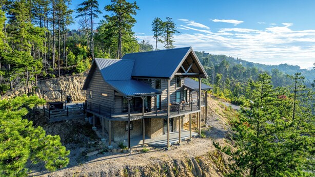 Een houten blokhut met balkon, omringd door bomen en een rotsachtig landschap.