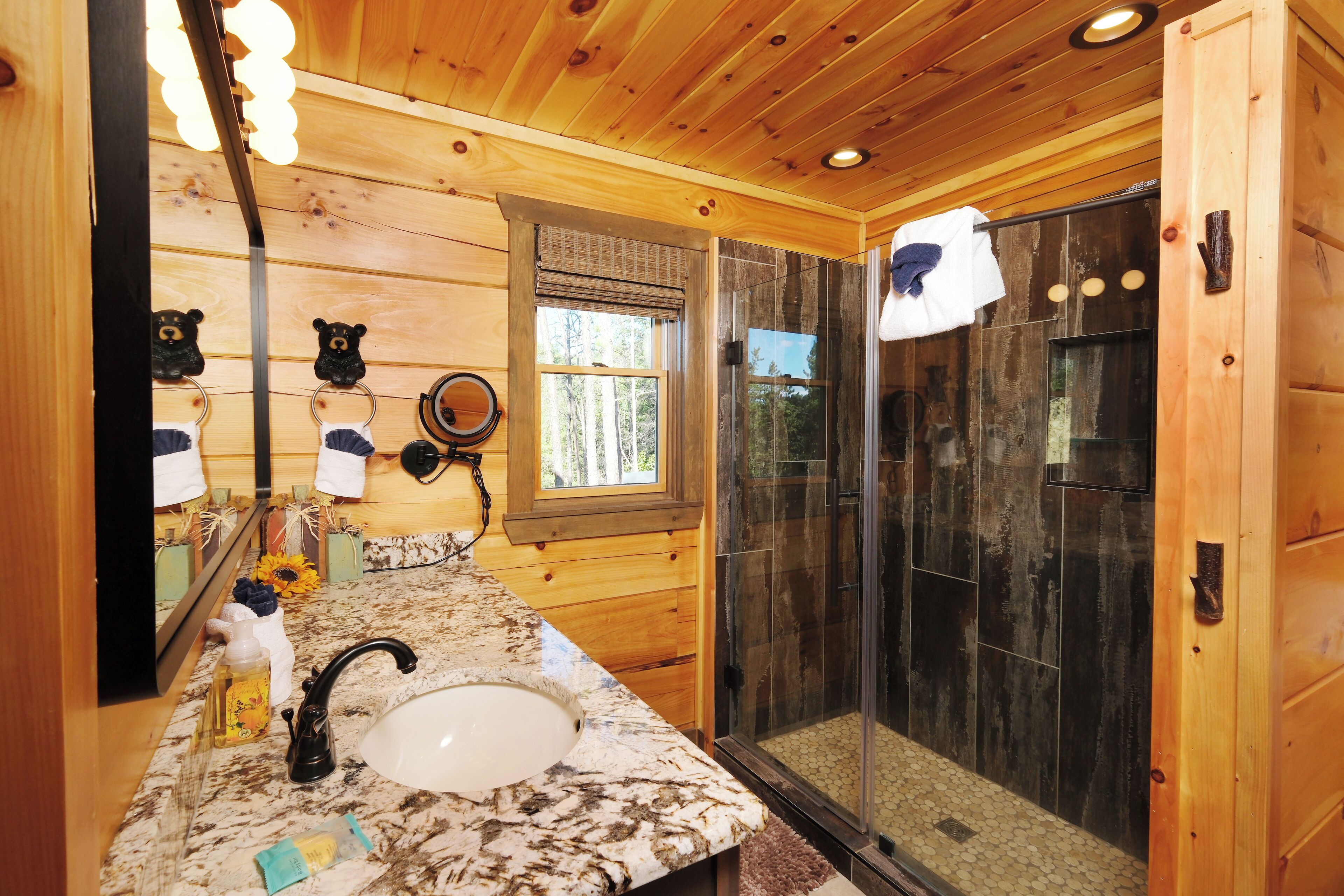 A wooden cabin bathroom with a marble sink, a glass shower enclosure, and a mirror with bear decorations.