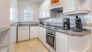 Una cocina con armarios blancos, encimera de granito, horno empotrado y cafetera.