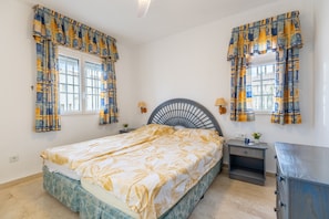 Ein Schlafzimmer mit einem Bett, zwei Nachttischen, einer Kommode und Vorhängen.