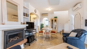 Una sala de estar con chimenea, comedor, sofá de cuero negro y televisor.