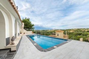 Ein Schwimmbad mit Blick auf die Landschaft, eine überdachte Terrasse und eine Steinskulptur.
