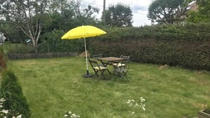 Un patio trasero con césped, una mesa y sillas de madera bajo un paraguas amarillo.