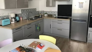 Una cocina moderna con armarios grises, un refrigerador de acero inoxidable, un lavamanos y una cafetera.