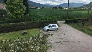 Un paisaje rural con un camino de grava que conduce a un coche blanco aparcado cerca de una casa.