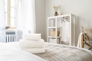 Ein ordentlich bezogenes Bett mit gefalteten weißen Handtüchern, ein weißer Kleiderschrank und ein Heizkörper im Hintergrund.