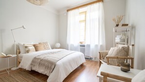 A bedroom with a bed, bedside table, lamp, chair, and a shelf with books and decorative items. - Cozy and peaceful studio apartment (Helsinki)