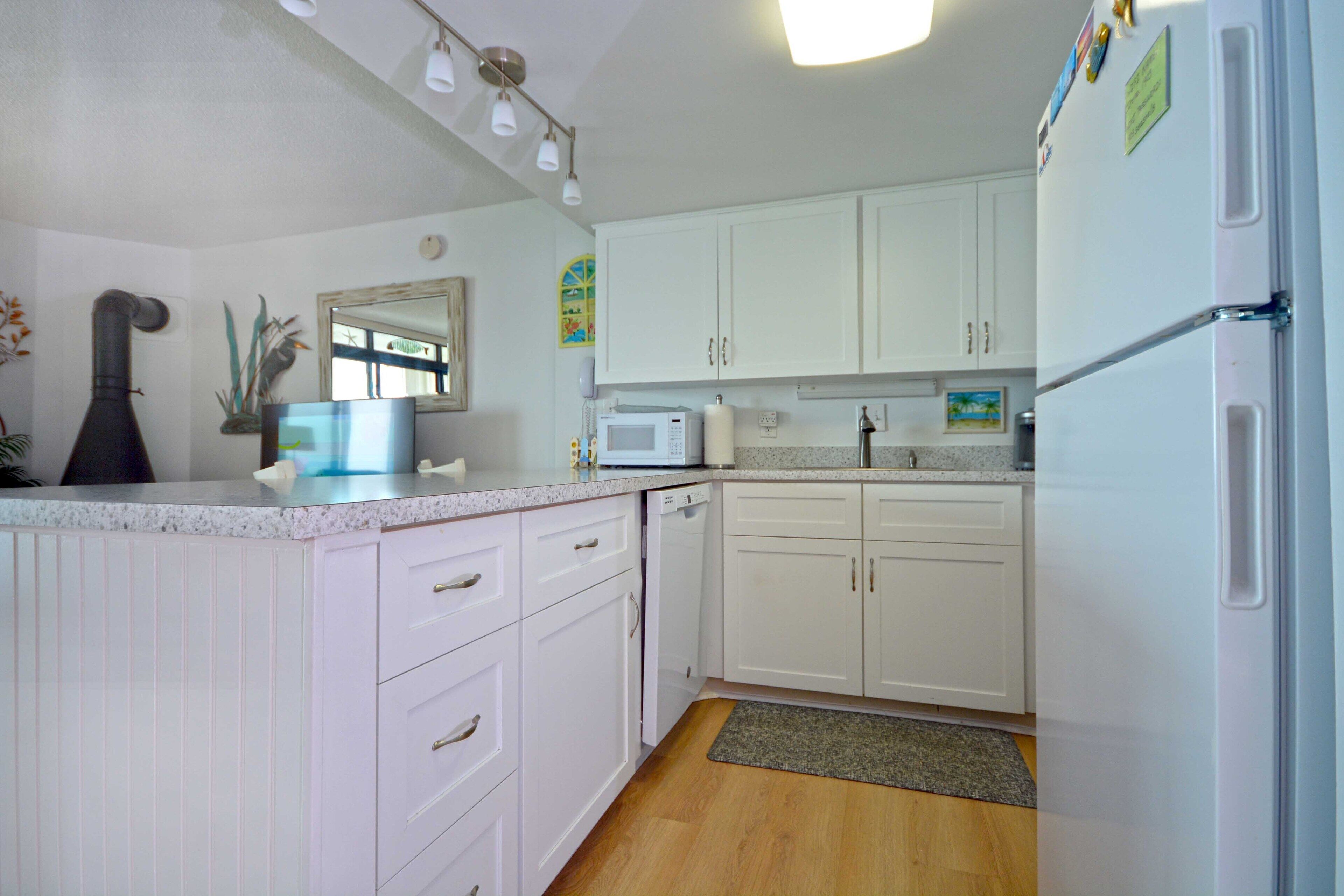 A kitchen with white cabinets, a microwave, a refrigerator, and a sink.