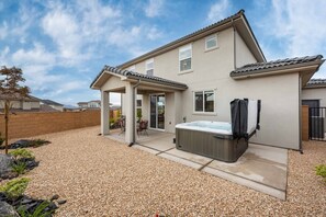 Une maison à deux étages dotée d’un patio couvert, d’un jacuzzi et d’une allée en gravier.