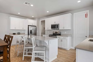 Une cuisine moderne avec des meubles blancs, un îlot central, des appareils en acier inoxydable et un coin repas avec des chaises blanches.