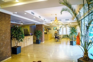 A hotel lobby with a reception desk, seating area, large chandelier, and potted plants.
