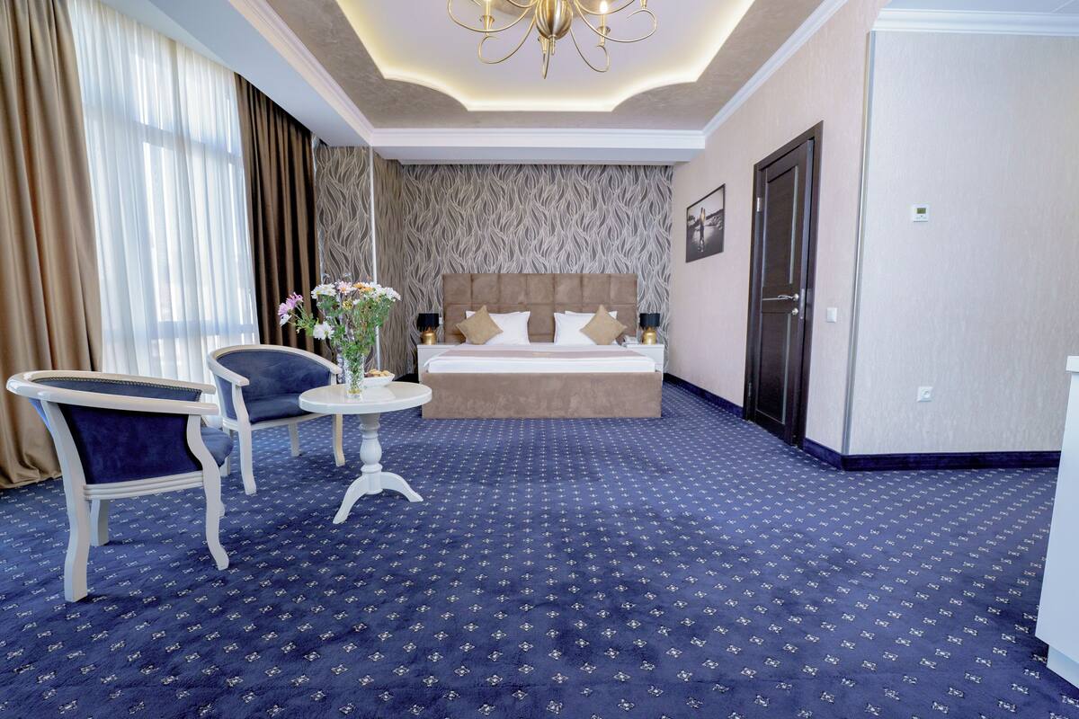 Ein Hotelzimmer mit Bett, einem Sessel, einem kleinen Tisch und einer Blumenvase.