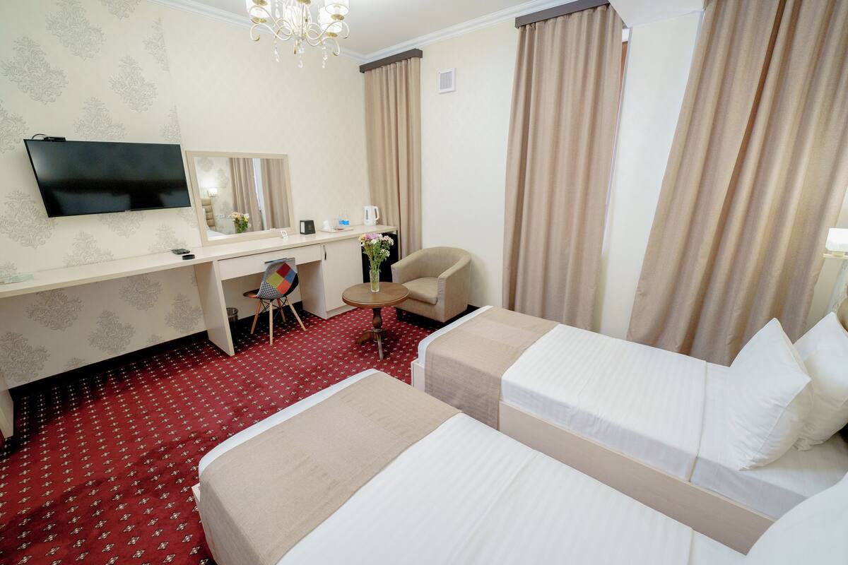 Ein Hotelzimmer mit zwei Betten, einem Schreibtisch mit Fernseher, einem Sessel, einem kleinen Tisch und einem Spiegel.