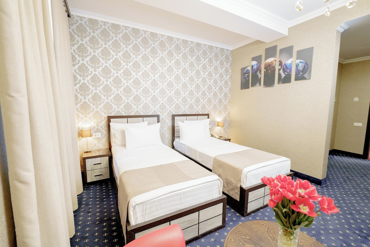 Ein Hotelzimmer mit zwei Betten, einem kleinen Tisch, einer Vase mit Blumen und floraler Wandgestaltung.