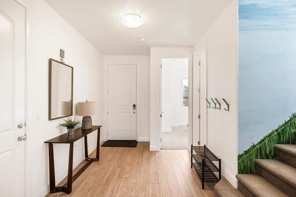 A hallway with a wooden floor, a dark console table with a lamp, a mirror, and a door leading to another room.