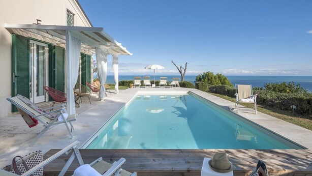 A pool area with a view of the sea, lounge chairs, and umbrellas. - Villa Lucente 6 2 (Silvi)