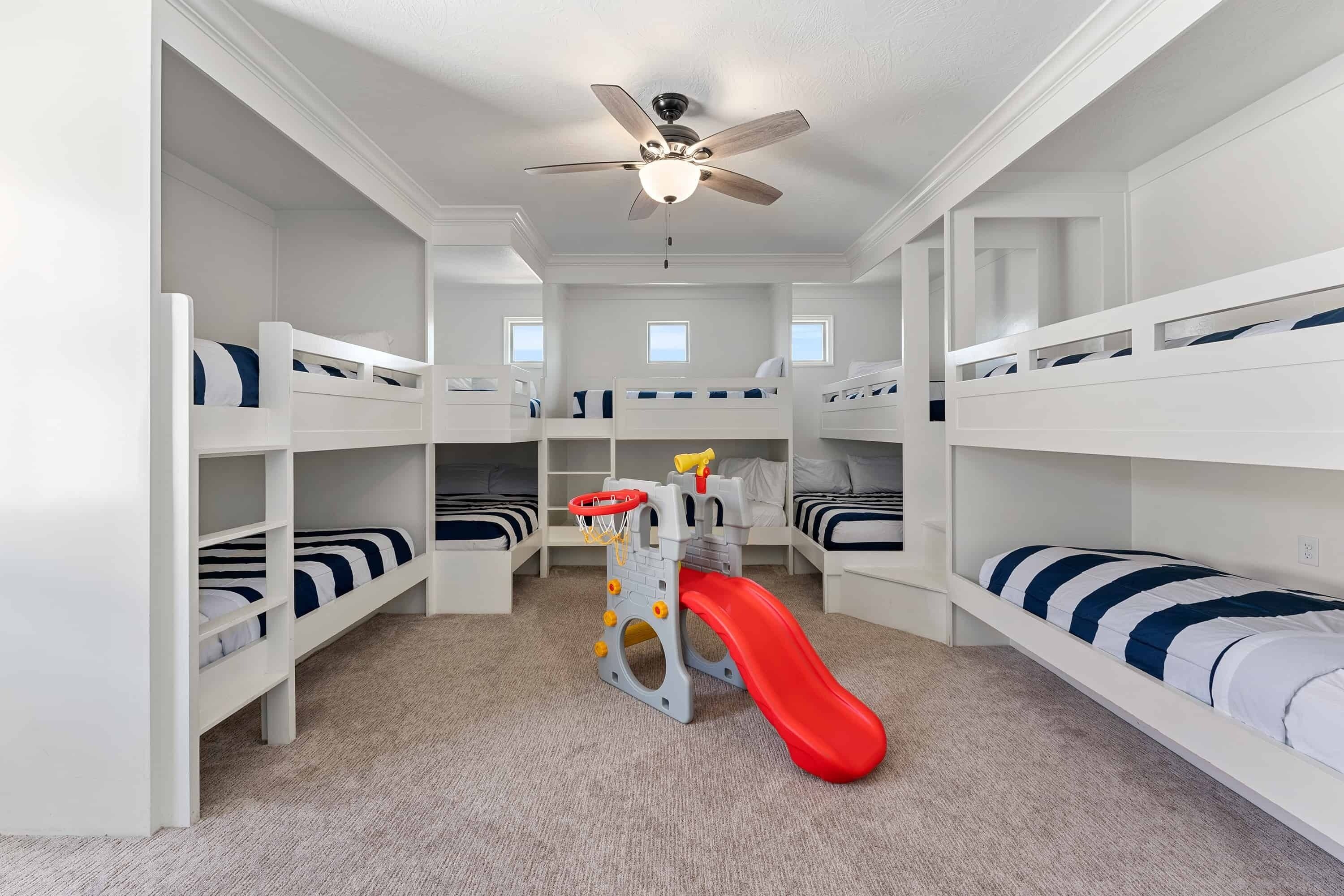 Une salle de jeux pour enfants avec des lits superposés, un toboggan et un ventilateur de plafond.
