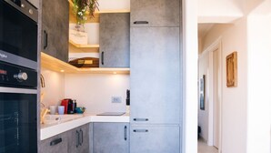 Uma cozinha moderna com armários cinzas, forno embutido e bancada com cafeteira e xícaras.