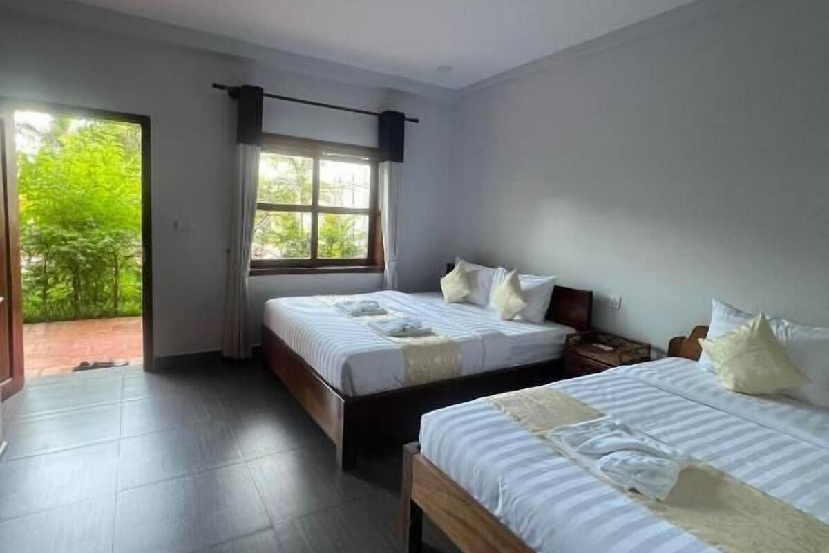 Een hotelkamer met twee bedden, een groot raam en uitzicht op groen.