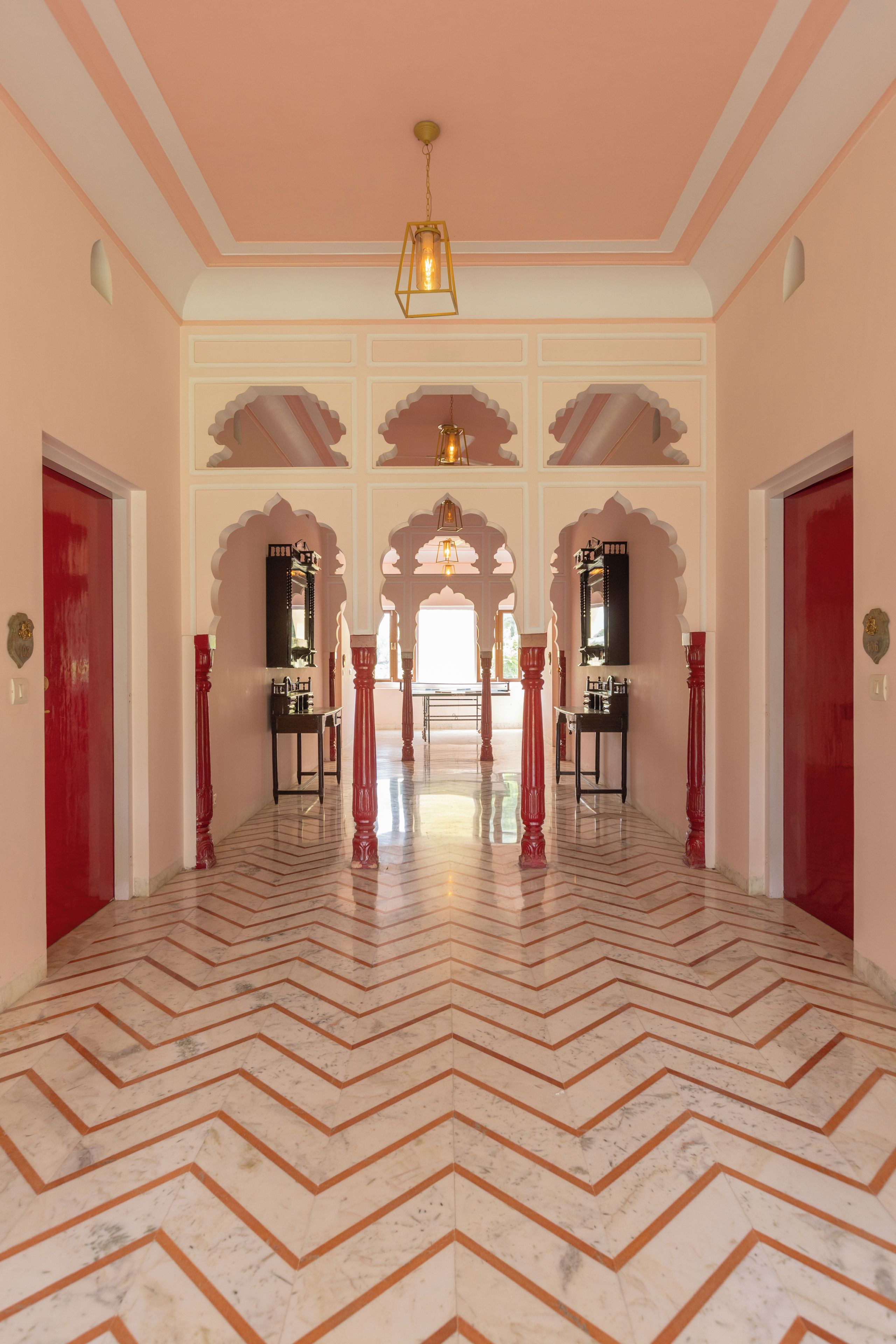 A corridor with a herringbone floor pattern, ornate arches, and a central chandelier.