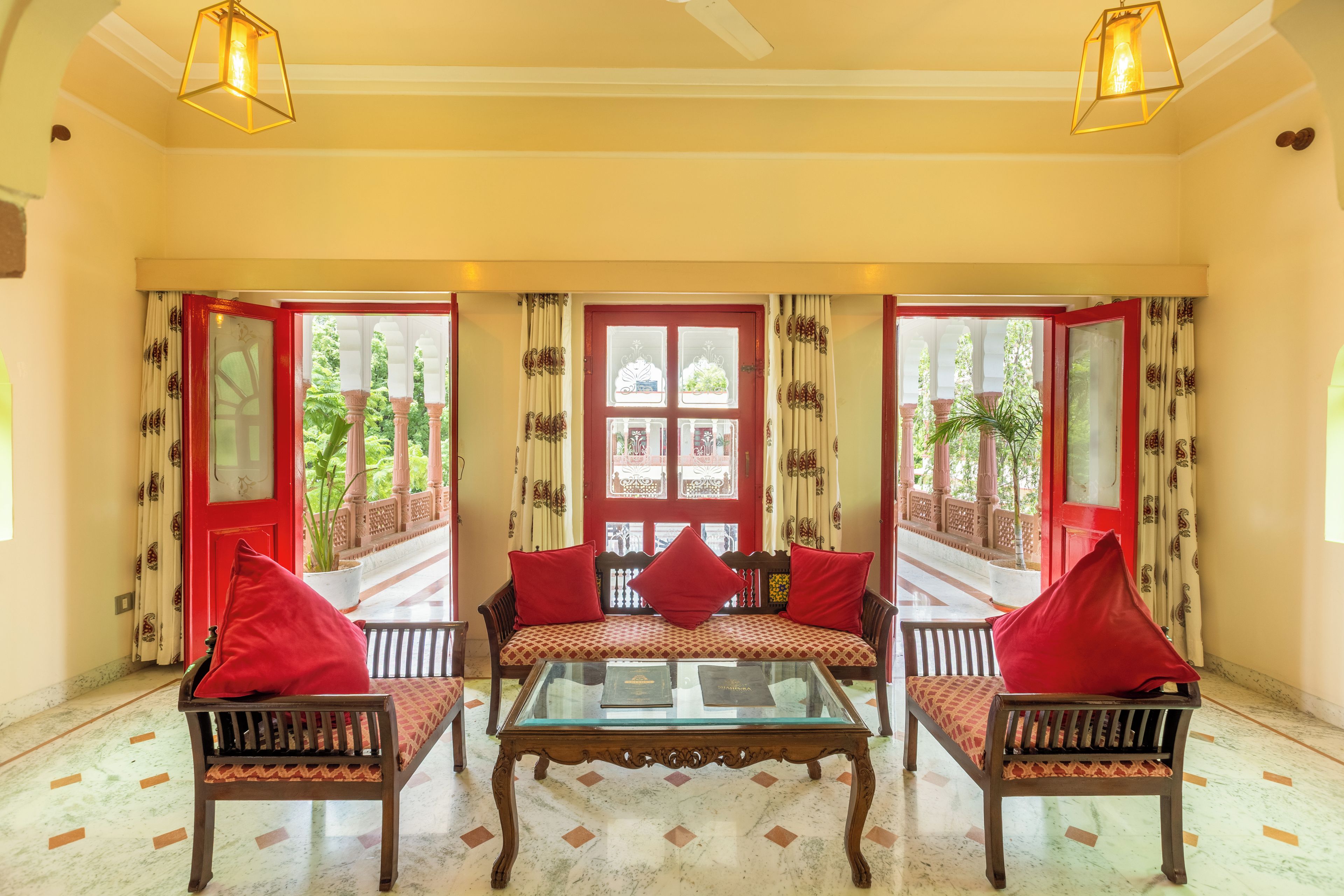 A room with a glass-top table, two sofas with red cushions, and a red door with decorative glass panels.