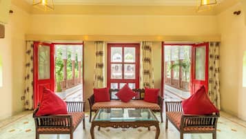 A room with a glass-top table, two sofas with red cushions, and a red door with decorative glass panels.