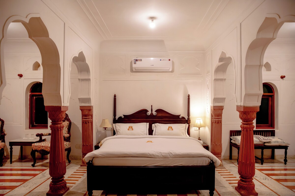 Un dormitorio espacioso con una cama grande, pilares de madera ornamentados y un diseño clásico.