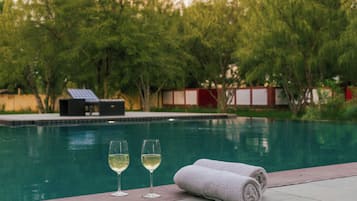 Una piscina con dos vasos de vino blanco y una toalla enrollada en el borde.
