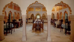 A spacious dining hall with multiple tables and chairs, ornate arches, and a central chandelier. - Shahpura Abhaneri Resort (Baswa)