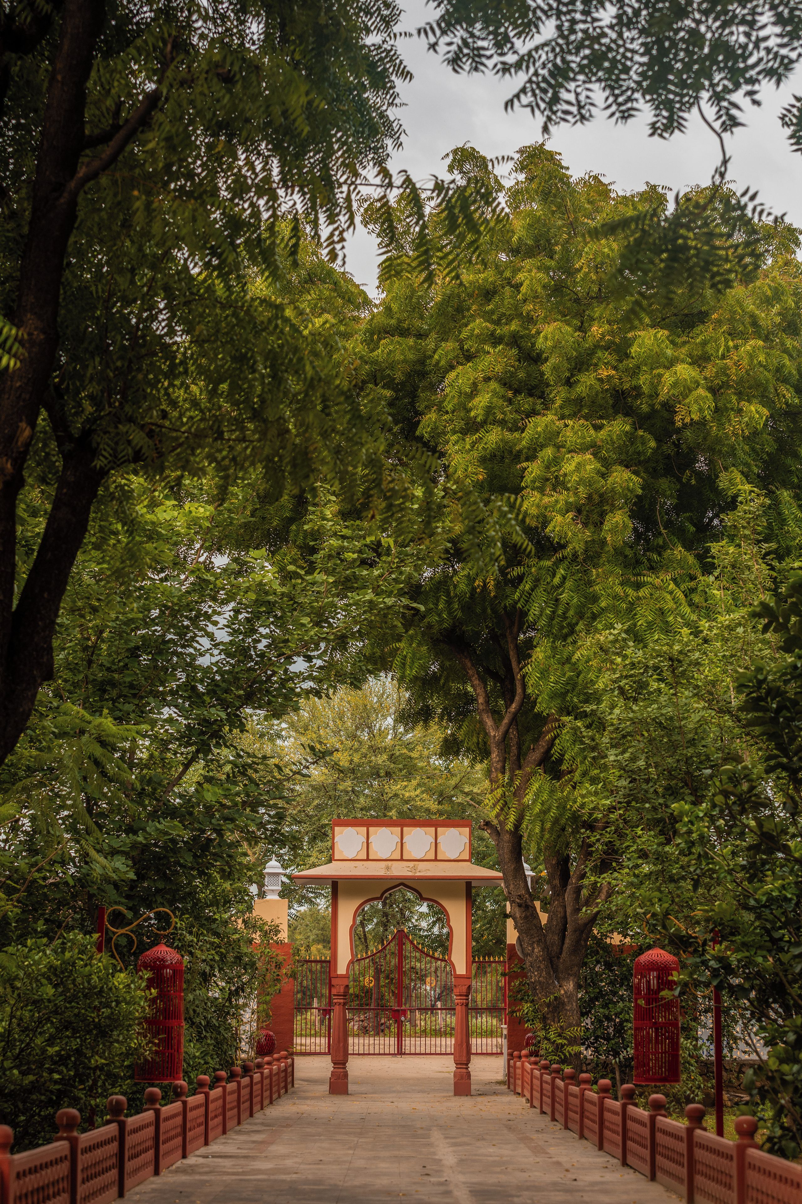 Un arco tradicional con un portón rojo, rodeado de frondosos árboles verdes.