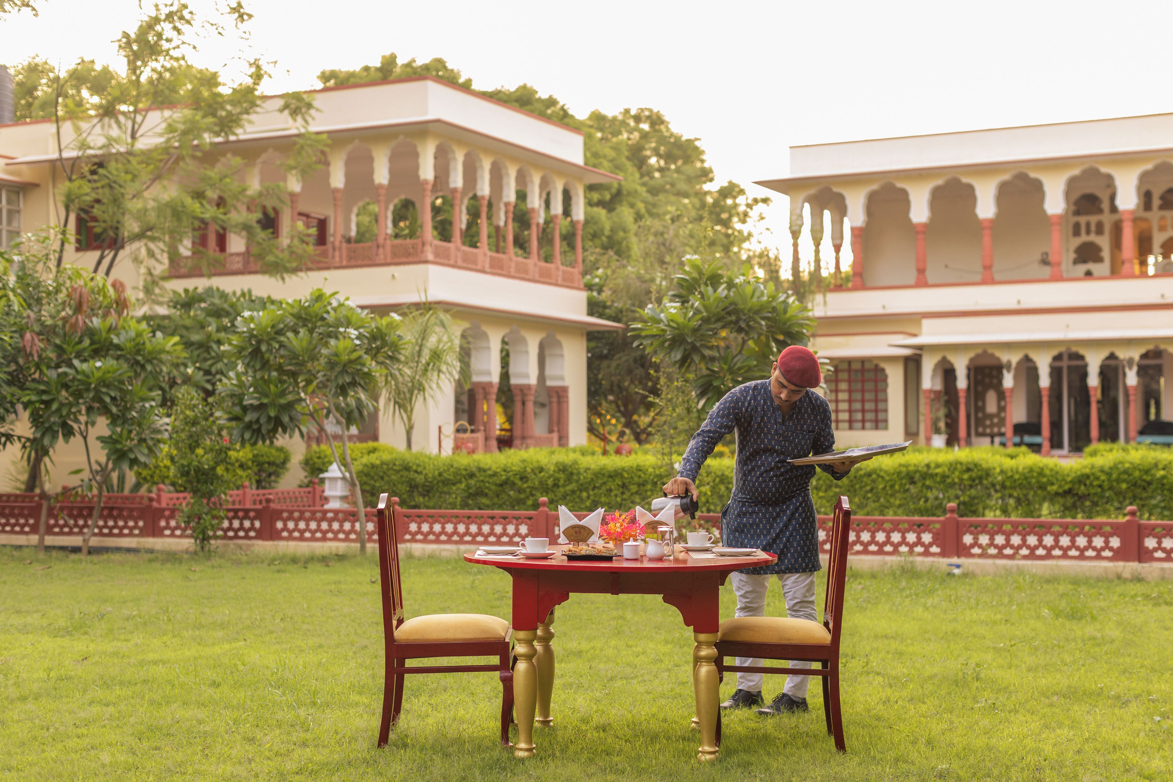 A person serving tea at an outdoor table with a view of a large building with arches.