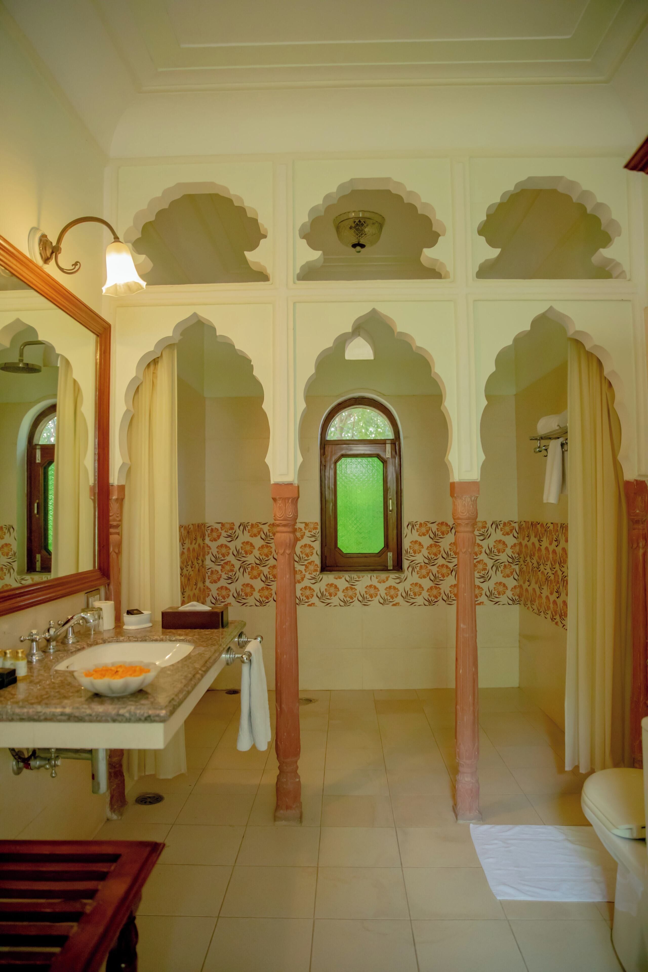 A bathroom with a marble sink, a mirror, a window with a green glass pane, and decorative arches.