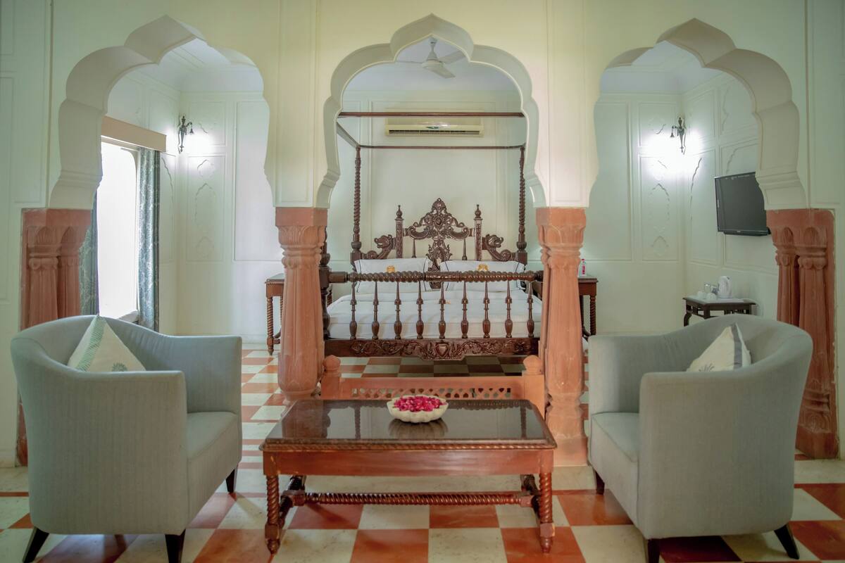 A traditional room with a four-poster bed, two armchairs, and a small table with a flower centerpiece.
