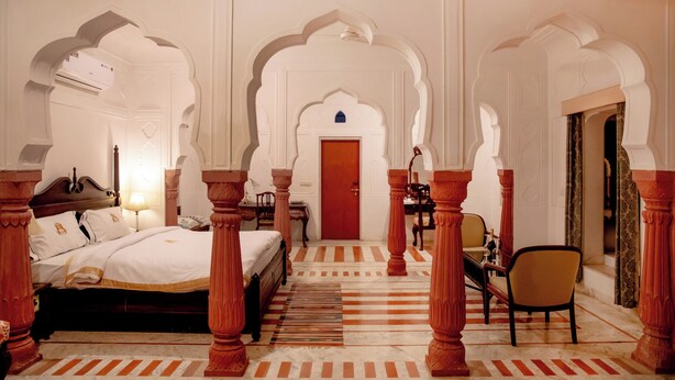 A traditional room with a bed, a desk, and a chair, featuring ornate arches and a patterned floor. - Shahpura Abhaneri Resort (Baswa)