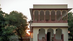 A two-story building with a balcony, arched doorways, and a garden in the foreground. - Shahpura Abhaneri Resort (Baswa)