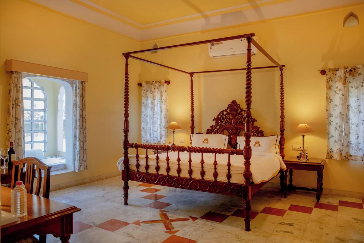 A four-poster bed with a wooden frame, a marble floor with a geometric pattern, and a window with floral curtains.