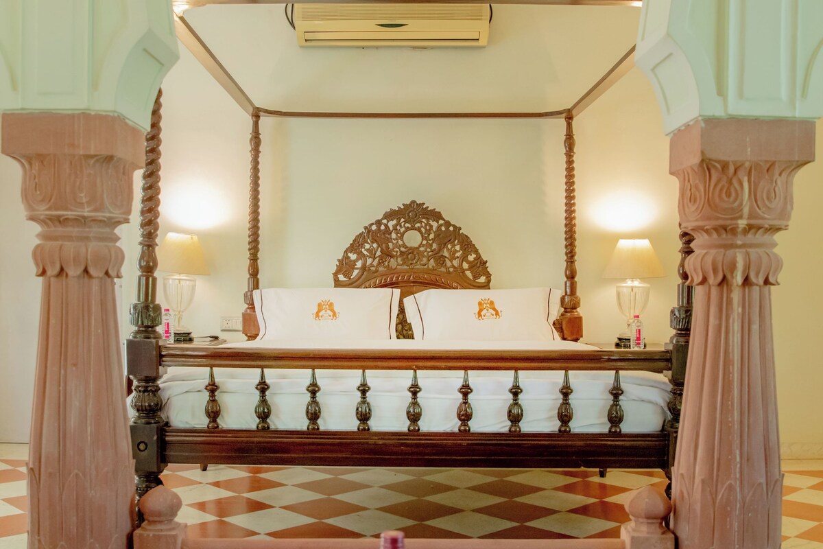 A room with a bed, a table with two wine glasses and a bottle, and a decorative ceiling fan.