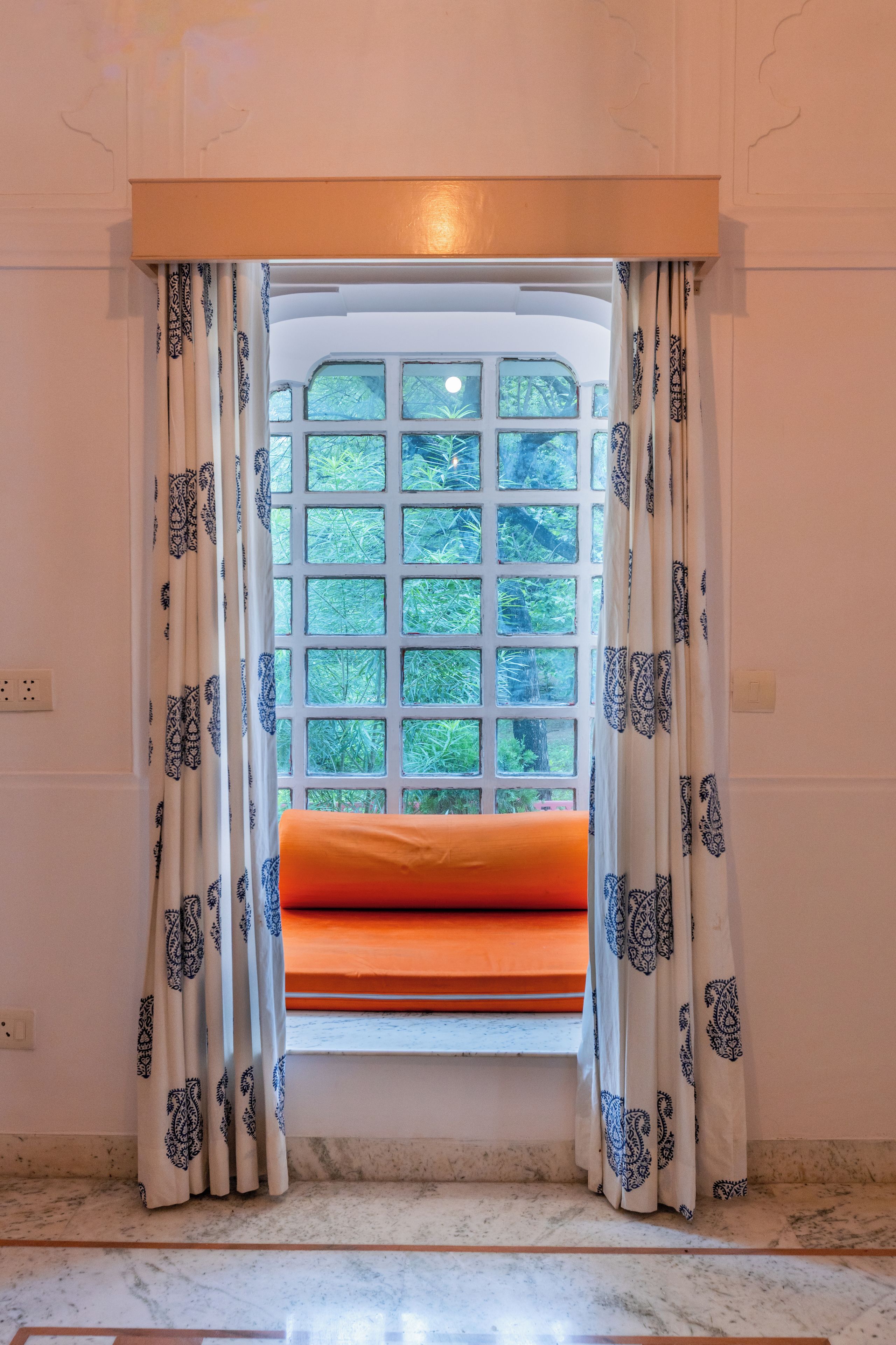A room with a window featuring a grid of glass panes, curtains with a paisley pattern, and a cushion on the window sill.