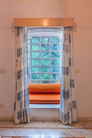Una habitación con ventana que tiene un entramado de vidrios, cortinas con estampado de hojas de parra y un cojín en el alféizar.