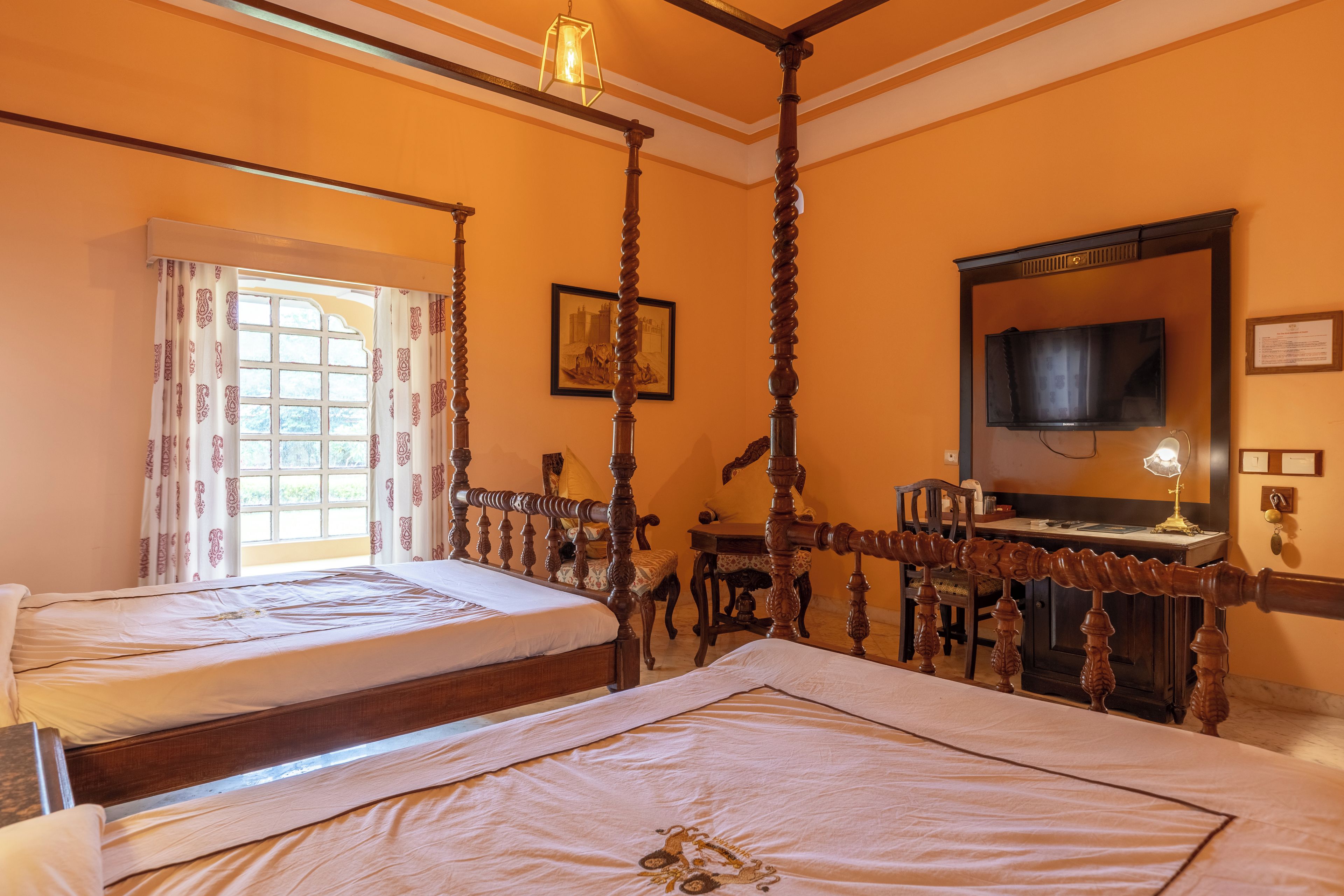A room with a four-poster bed, a desk with a chair, a television, and a window with curtains.