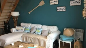 Una sala de estar acogedora con un sofá, una mesa de centro y una lámpara. Se observan adornos en la pared y una escalera al fondo.