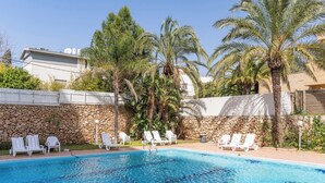 Piscina com cadeiras de sol brancas, palmeiras e um muro de pedra.