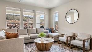 A modern living room with a sectional sofa, two armchairs, a round coffee table, and large windows offering a view of a rocky landscape.
