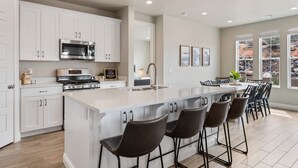 A modern kitchen with white cabinets, a stainless steel microwave, a stove, and a large island with bar stools.